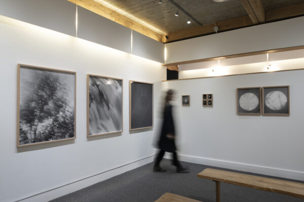 An art gallery with black and white photographs hanging on white walls and a person walking between exhibits.