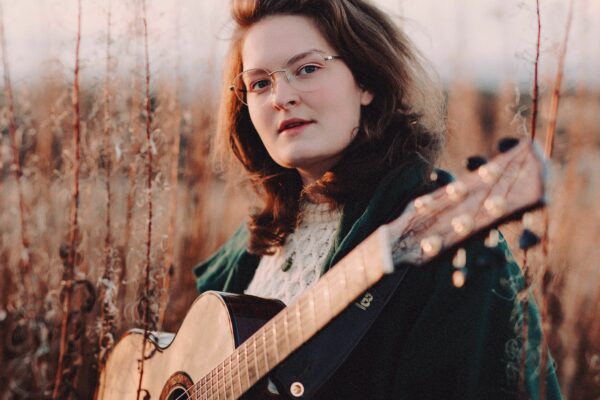 A woman stood in a field with a guitar